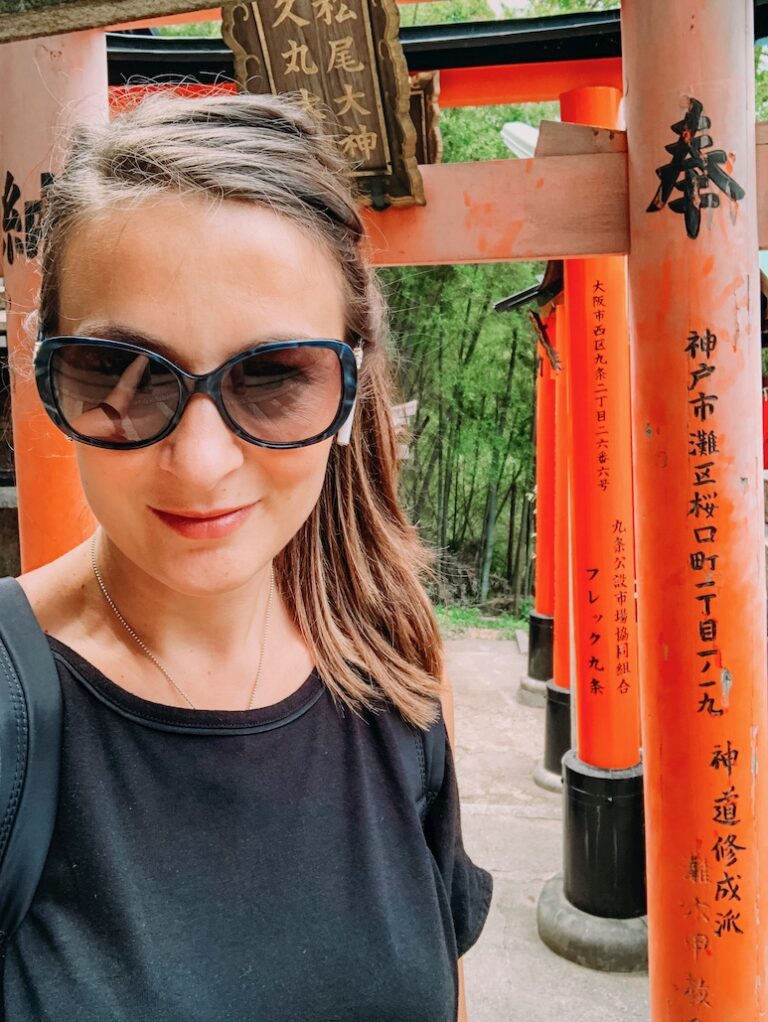 Bec is a Sydney travel blogger who travelled solo to Japan. Here she is walking through the red and black torii gates at the Fushimi Inari Shrine in Kyoto, wearing a black top and sunglasses
