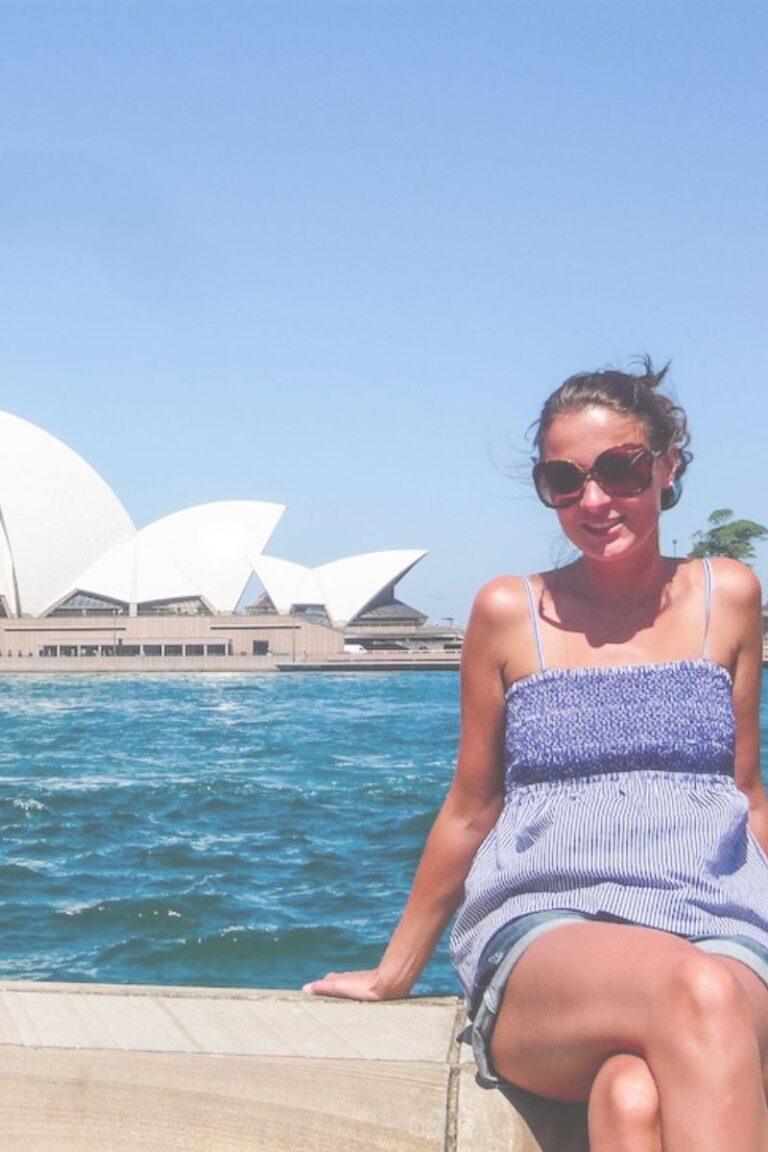 Travel blogger sitting in front of the Sydney Opera House in Sydney, Australia on a bright, sunny day.