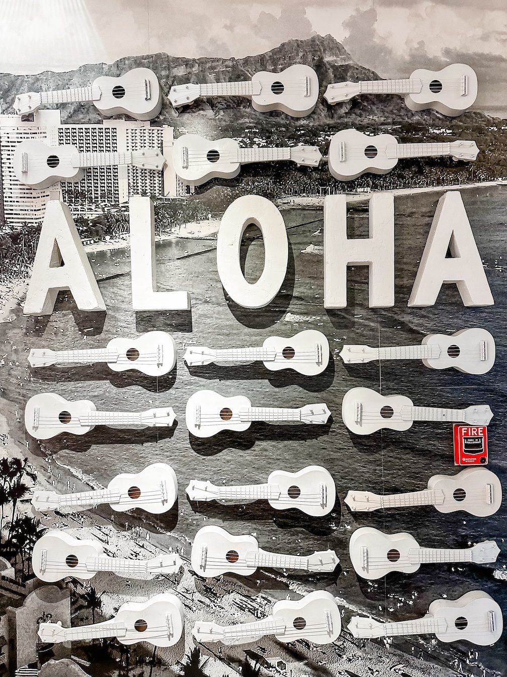 A wall of ukulele's spotted in a department store in Waikiki, Honolulu, Hawaii. The wall is a black and white photo of Waikiki Beach, with white ukuleles mounted over the top.