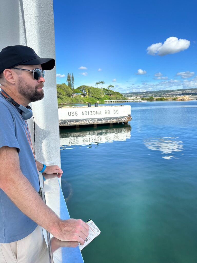 Chris Bowman visiting the USS Arizona Memorial at Pearl Harbour, Hawaii. The sky is bright blue with only a few white clouds, the water us just as blue as the sky.