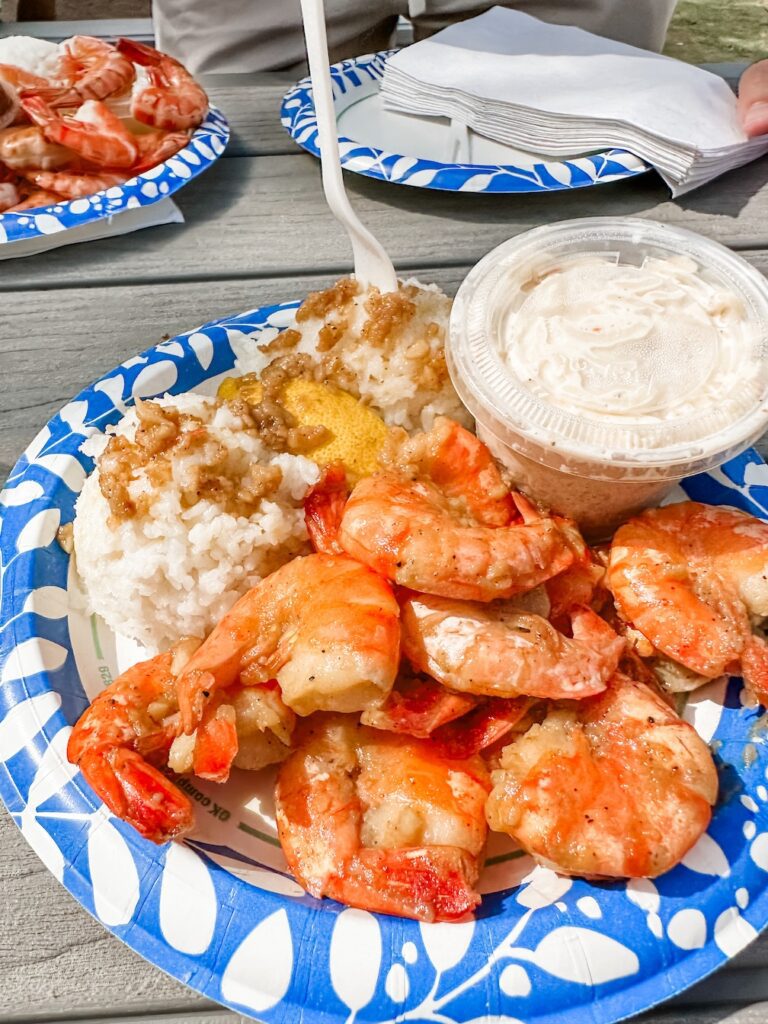 Photo shows a disposable plate of garlic shrimp from Giovanni's Shrimp Truck in Oahu, Hawaii. There is a heap of fried garlic shrimp with two scoops of rice, garlic sauce and homemade Mac n cheese on the side.
