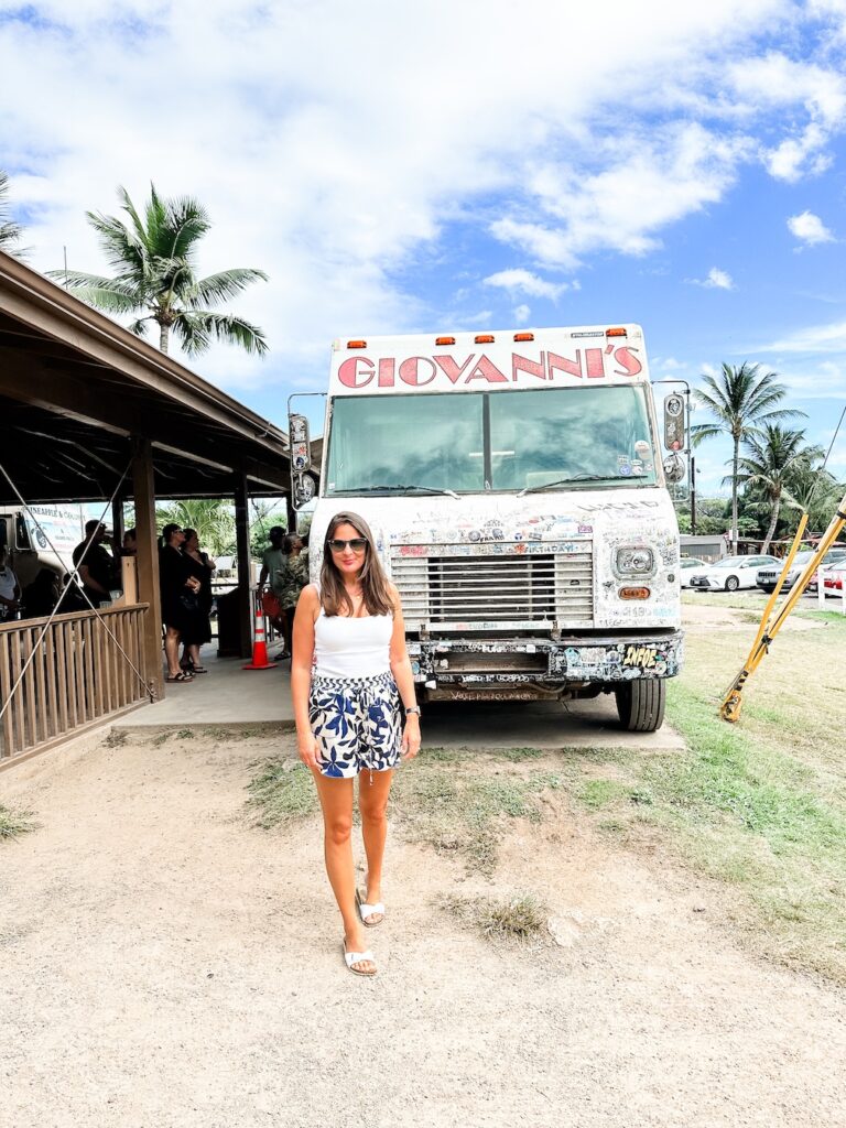 Sydney travel blogger, Bec Bowman stands in front of Giovanni's shrimp truck in Oahu, Hawaii. The sky is blue with white clouds, the van is white with the name 'Giovanni's' in large red letters.