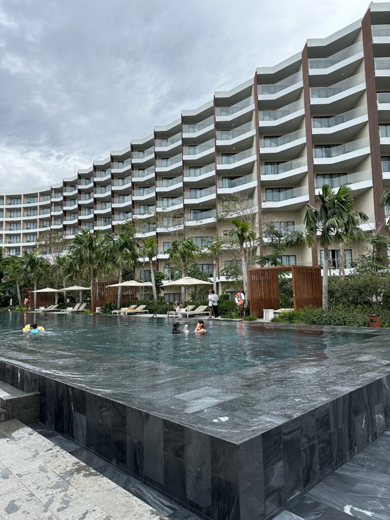 View of the pool at Crowne Plaza Phu Quoc Starbay. The sky is overcast, but the palm lined pool is inviting. 