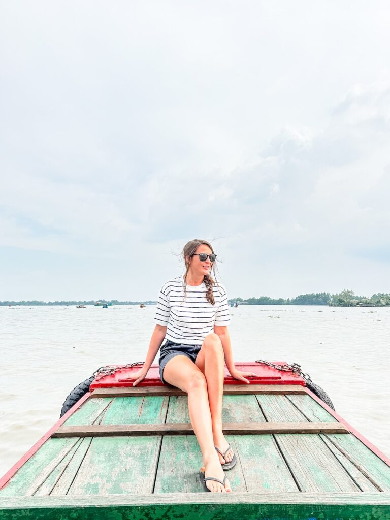 A woman sits on the front of a motorboat as it passes along the Mekong River in Vietnam. She is smiling, wearing a striped t shirt and shorts.